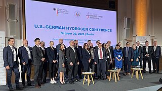 A big group of people in business attire standing on a stage with screens in the background.