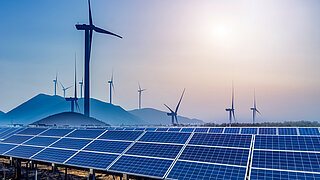 Solar panels in the foreground, wind turbines in the background.